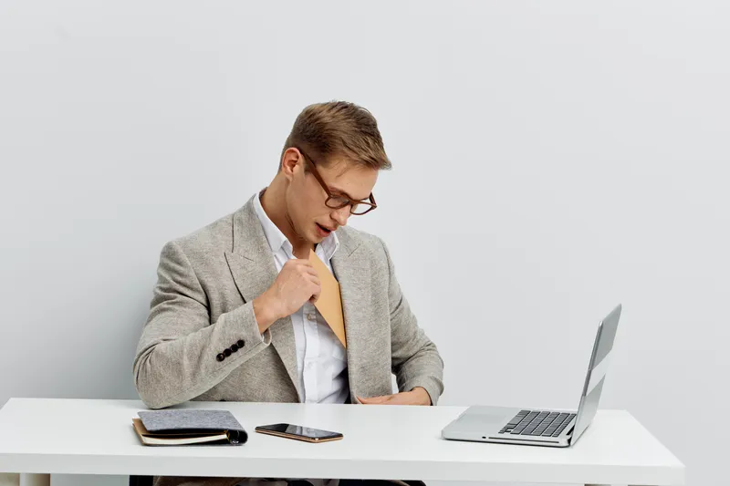 Professional young man in smart casual attire working with a laptop, smartphone, and notepad at office desk, looking at his watch, indoor workplace scene, modern environment, business lifestyle concep