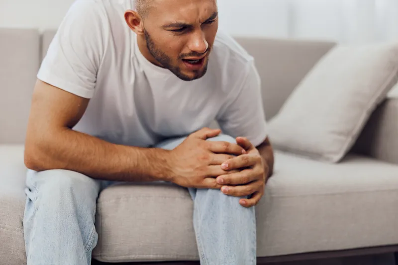 Worried man sitting on couch, experiencing anxiety about life and work balance while navigating emotional challenges in a digital age.