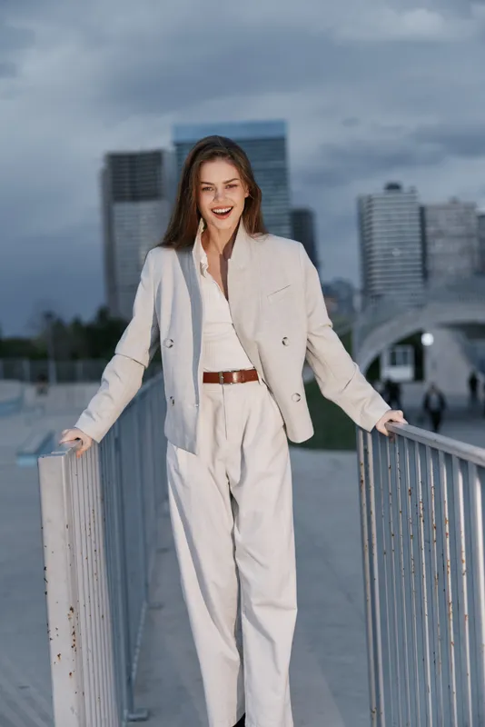confident business woman standing outdoors in light suit with urban background smiling during cloudy day financial crisis concept