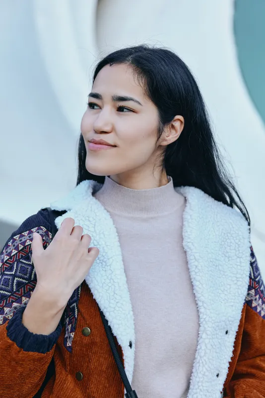 Woman wearing a brown shearling coat over a soft knit sweater outdoors, casual fashion style, confident pose, urban backdrop, soft natural light, contemporary streetwear vibe and atmosphere