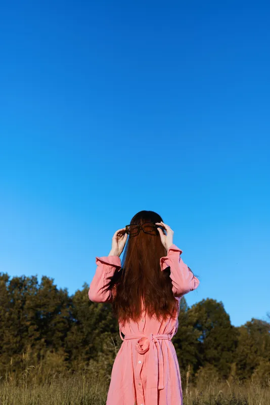 Young woman in a pink dress enjoying nature against a clear blue sky, representing freedom and tranquility in a rural setting
