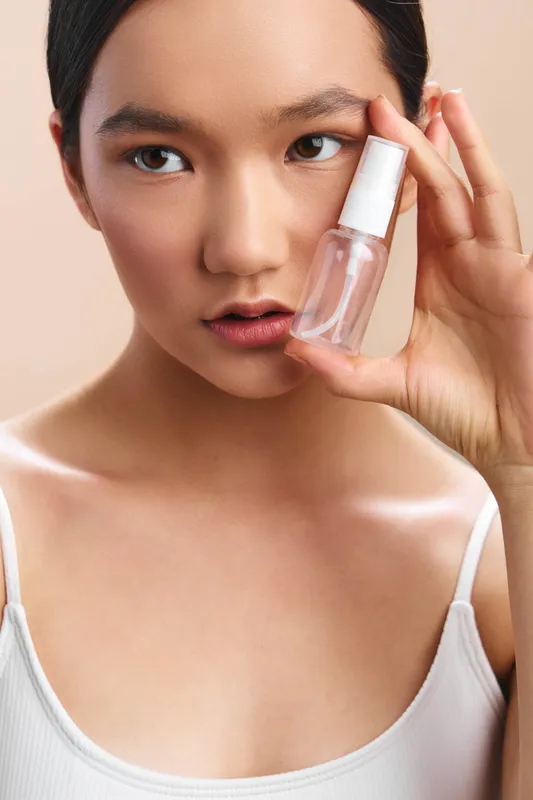 Asian woman applies skincare spray in a closeup beauty shot, highlighting clear skin and a focused expression. Soft lighting enhances a fresh, modern personal care moment and serene skincare routine.