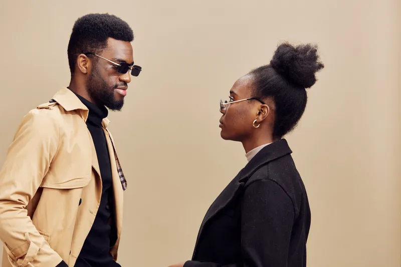 Stylish couple in sunglasses, wearing modern outfits, showcasing confidence and connection against a light brown background with a contemporary vibe