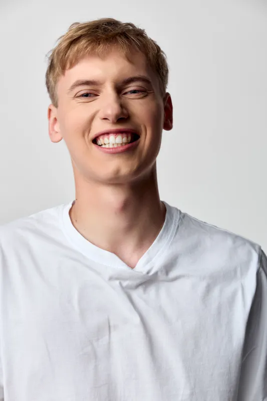 Smiling young man in a white shirt conveys a warm, approachable vibe for lifestyle, fashion or social media projects. Bright expression and casual style suitable for upbeat marketing and friendly