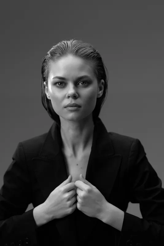 Black and white portrait of a serious woman in a dark jacket with a solid background.