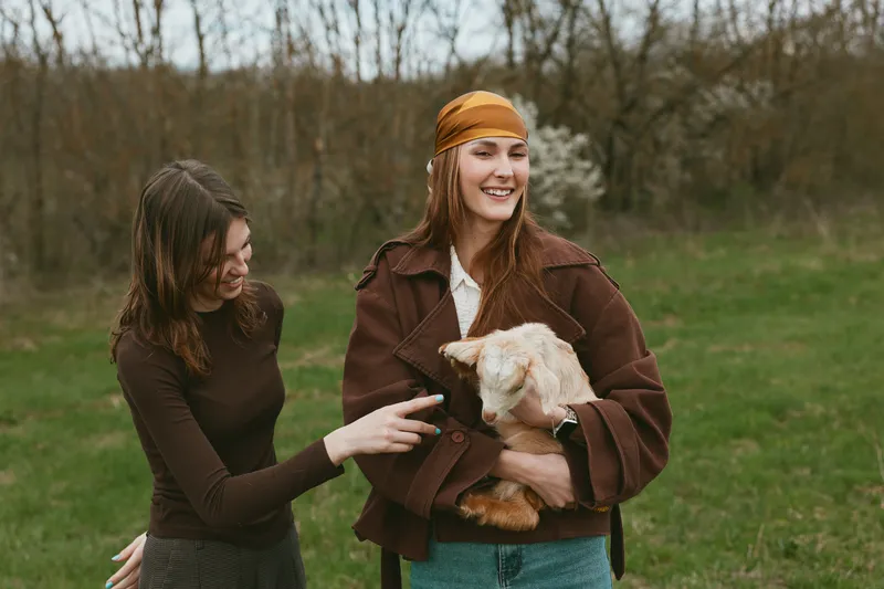 Cheerful women outdoors, smiling and relaxed, warm jackets, sunlit park setting, gentle breeze, natural colors, candid moment, friendly vibe, simple lifestyle, shared joy