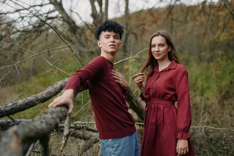 Warm authentic outdoor portrait of a young couple by fallen branches in a meadow, showing a genuine connection, relaxed posture, candid faces and credible unposed interaction.