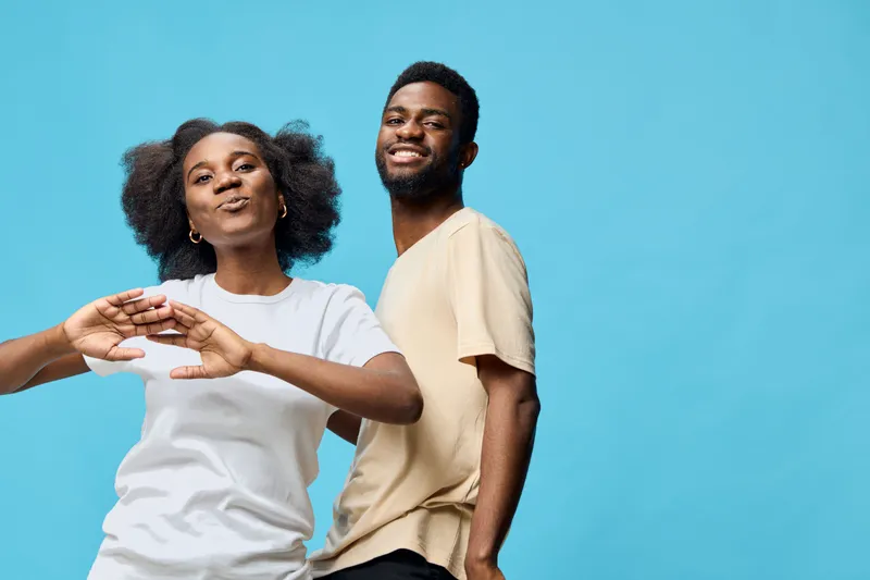 Happy African American couple dancing together in casual clothes with a blue background, expressing joy and positivity through their body language and smiles