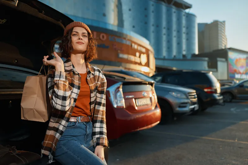 Woman shopping by car trunk in urban parking lot at golden hour, candid lifestyle portrait capturing authenticity, golden hour glow and mindful living with emotional storytelling and relaxed weekend