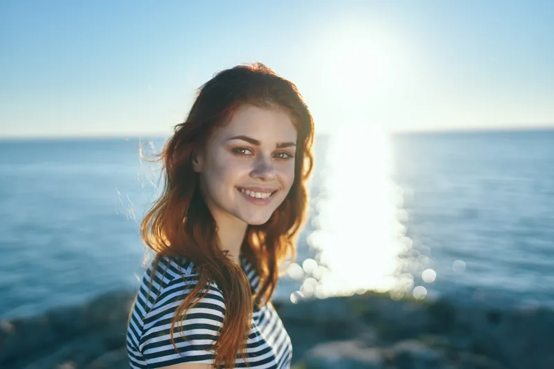 Счастливая женщина в футболке на закате у моря в горах