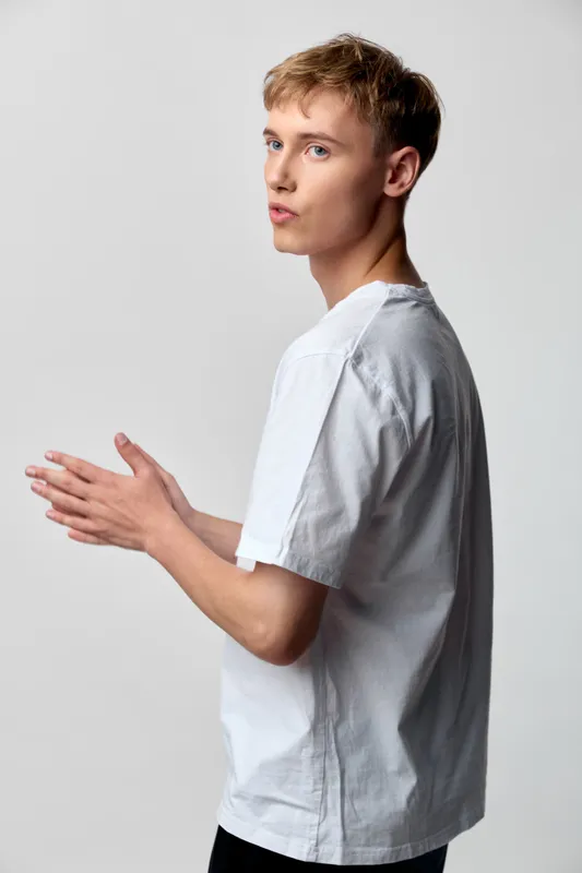 Man in a white t shirt clap gesture with a playful expression in a clean studio setting, showcasing casual style and dynamic communication for lifestyle, fashion, or advertising imagery