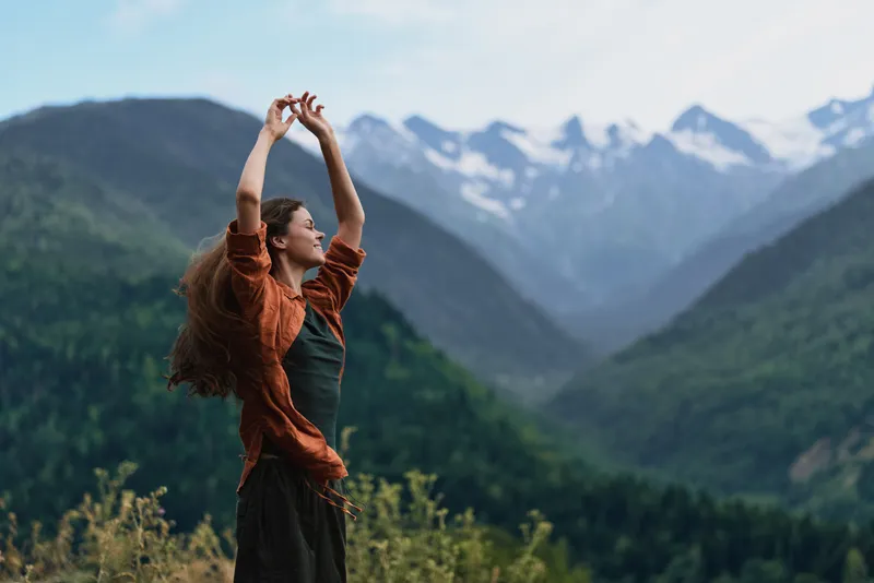 Woman standing in a mountainous landscape, arms raised in celebration, enjoying fresh air and vast scenery, evoking freedom, joy, and connection with nature in openness