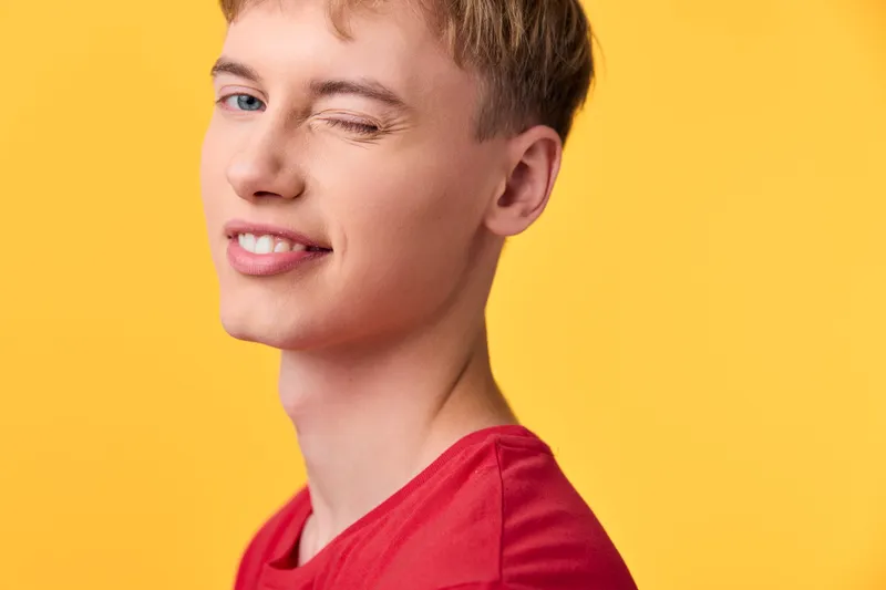 Smile and wink on a youth wearing a red shirt against a bright yellow background, conveying playful charm and lighthearted mood for lifestyle and fashion themed projects