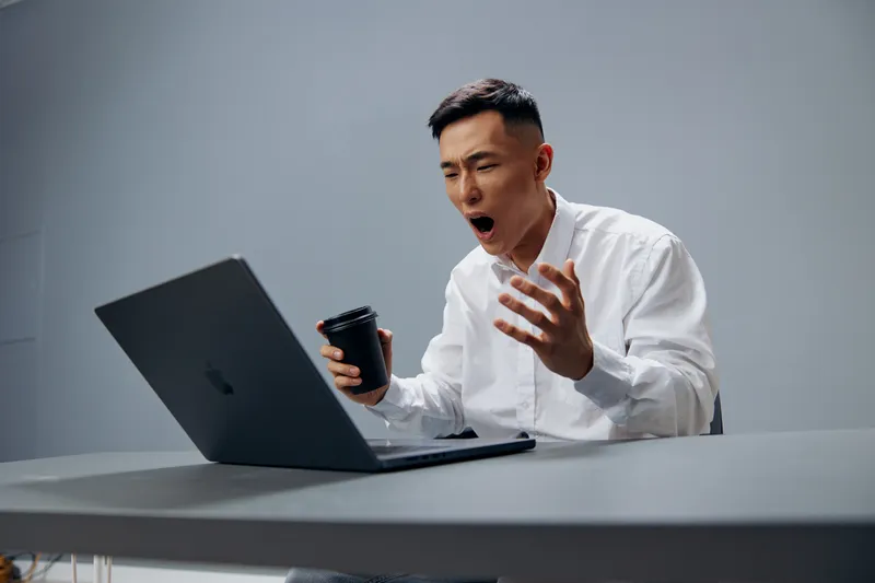 Менеджер в белой рубашке с чашкой кофе сидит перед ноутбуком