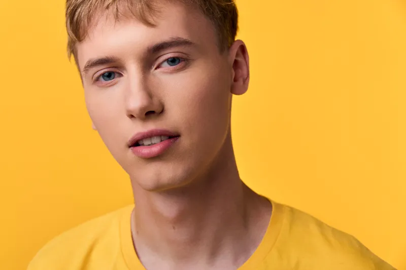 Close up of a young man wearing a bright yellow t shirt against a vivid yellow backdrop, studio lighting highlights smooth skin and a calm expression for a clean fashion oriented shot