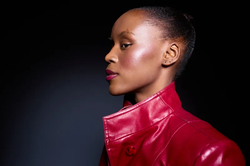 Profile of a confident black African woman with dark skin wearing a red leather jacket against a dark background. Concept of fashion, strength, and empowerment in portrait photography.