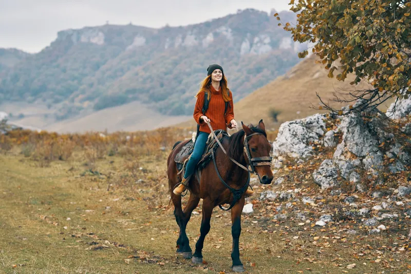 Женщина-туристка едет верхом на лошади в горах