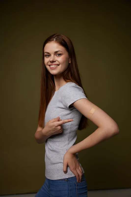 Симпатичная женщина указывает на руку, в которую была сделана вакцина от COVID-19, в спортивной студии