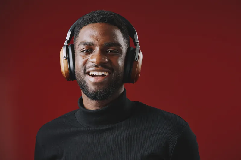 Happy young African American man wearing headphones, smiling in a cozy black turtleneck against a warm red background, conveying joy and music enjoyment