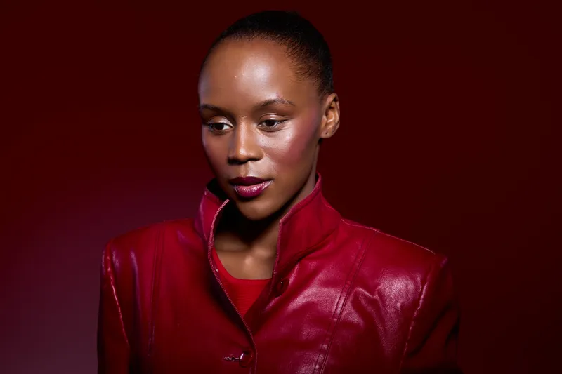 Portrait of a dark skinned African woman wearing a red leather jacket, looking down thoughtfully against a red background. Concept of fashion, beauty, and elegance.