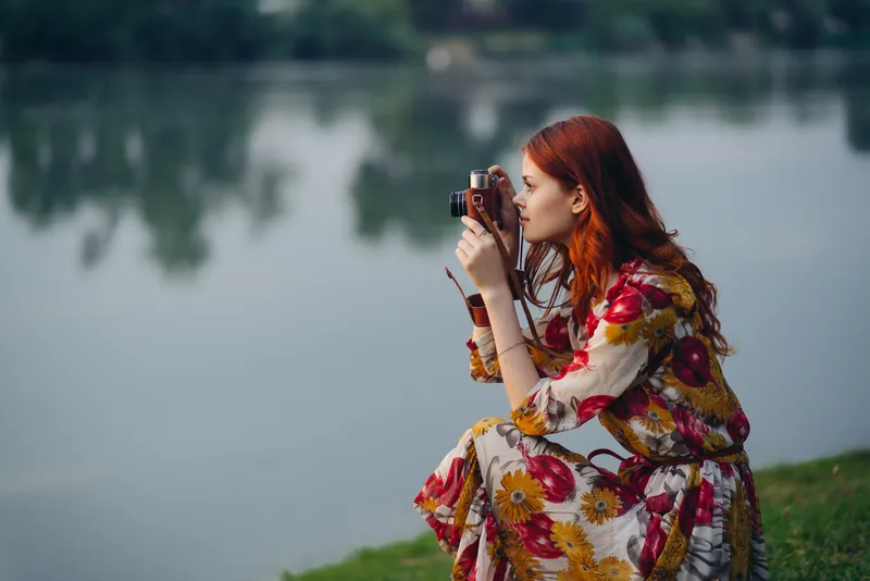 Симпатичная женщина с фотоаппаратом у озера, отдых на природе