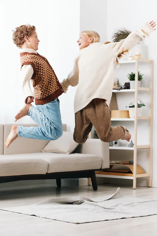 Authentic moment of playful joy in a cozy living room, featuring kids in a school themed game as they leap on a couch, capturing a carefree lifestyle scene.