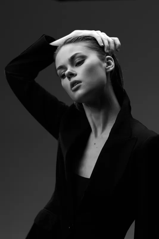 Black and white portrait of a thoughtful woman with closed eyes wearing a dark jacket in studio lighting.