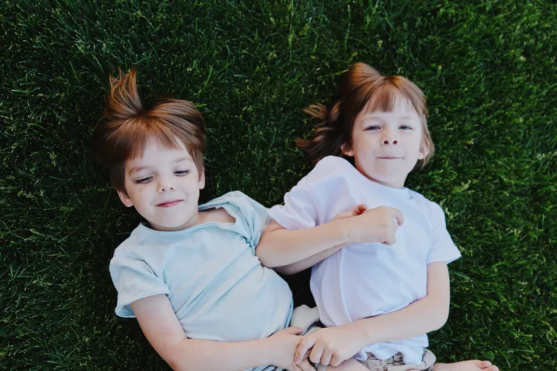 Enchanting children with playful expressions lying on green grass, showcasing innocence and joy. This image captures a moment of carefree childhood bliss.
