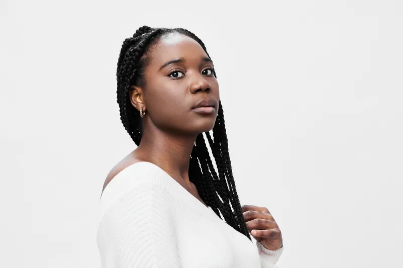 Portrait of a confident young African woman with braided hair wearing a white sweater against a minimalist background
