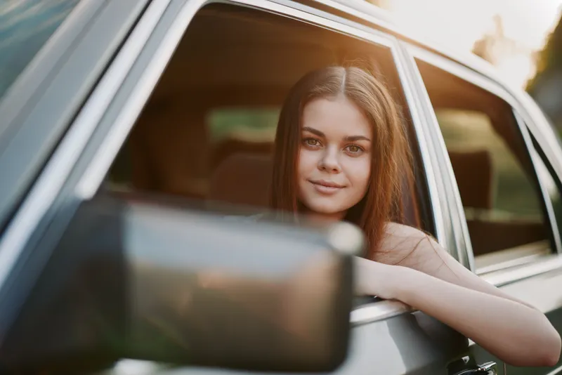 Young woman enjoying a summer road trip with beautiful sunlight shining through the car window, evoking a sense of freedom and adventure.
