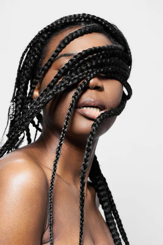 Artistic portrait of a Black woman with intricate braided hair covering her eyes, conveying deep emotion and uniqueness in a minimalist setting