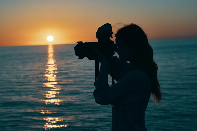 Женщина-фотограф с камерой на закате у моря, природный пейзаж