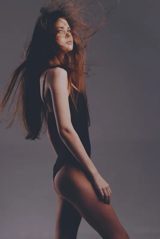 graceful woman with flowing hair in black bodysuit posing against dark background