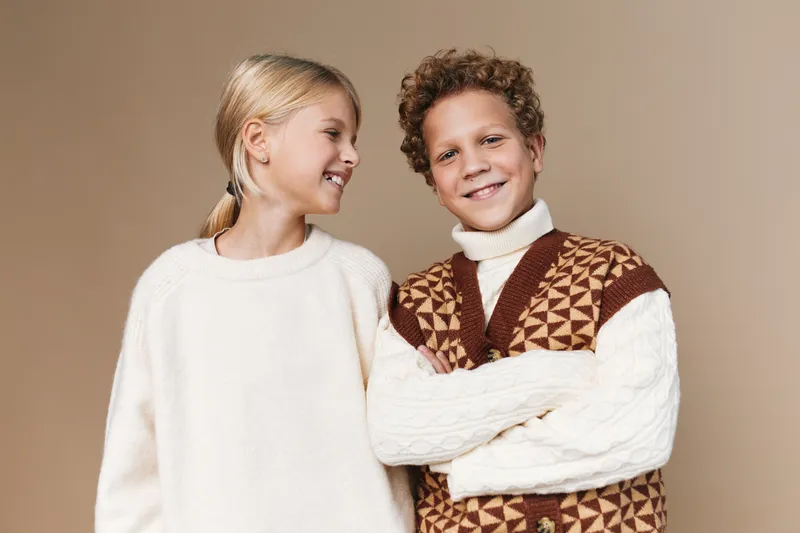 Authenticity shines in this school lifestyle moment, featuring two children in cozy knitwear, celebrating friendship, curiosity, and natural play in a warm studio setting with soft light.
