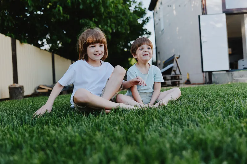 Happy children sitting on grass, enjoying a sunny day outdoors with bright smiles and playful energy in a relaxing environment filled with greenery.