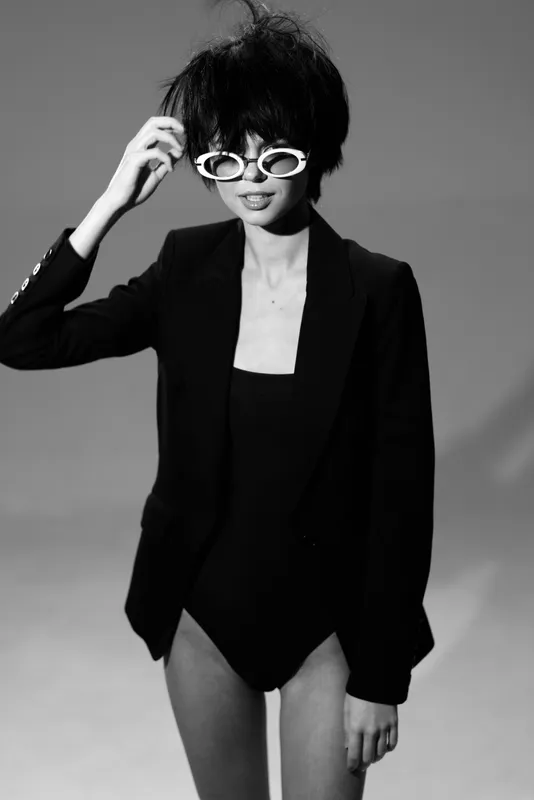 Black and white stylish woman wearing sunglasses and a blazer with confident expression in studio lighting.