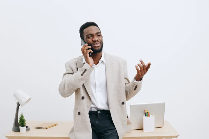 Confident man talking on mobile phone while standing at modern office desk against white background, professional male entrepreneur in smart casual attire, workplace communication, business success, p