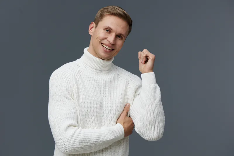 Smiling man in white sweater raise fist celebrate success isolated on gray background studio portrait digital nomad concept