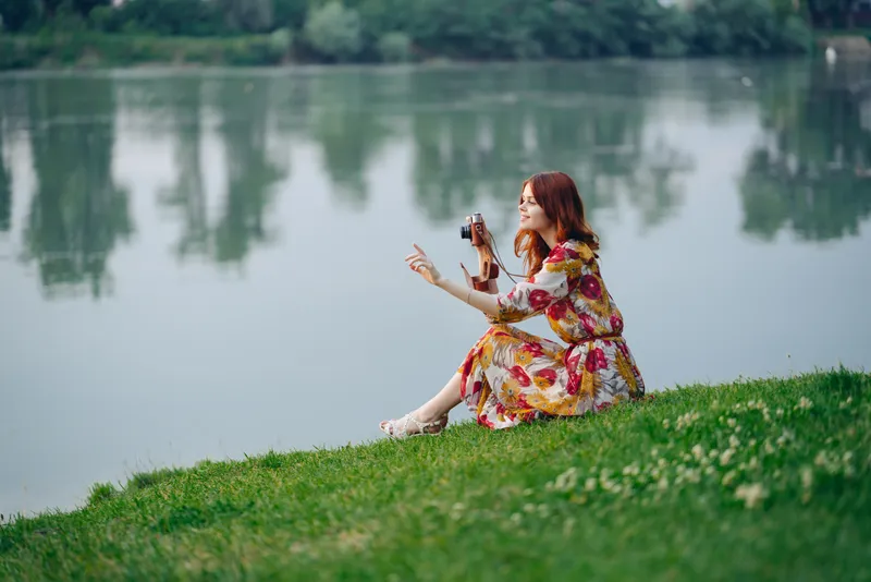 Симпатичная женщина в платье на открытом воздухе с фотоаппаратом в руках на фоне природы