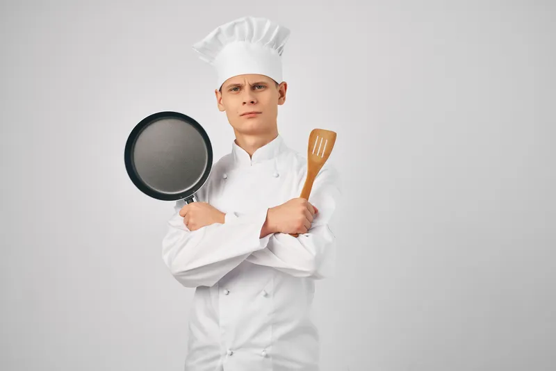 Повар с кухонной утварью, сковородой, работает, готовит