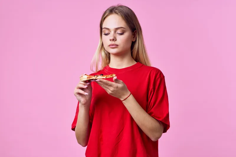 Женщина в красной футболке перекусывает фастфудом на розовом фоне