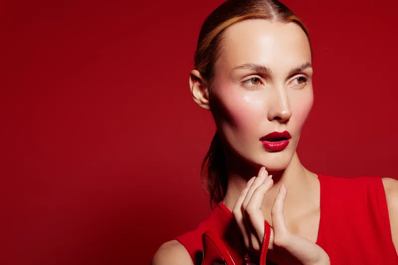 Portrait of a stylish woman with red lipstick and red dress posing against a red background. Concept of fashion, beauty, makeup, and elegance in studio lighting.