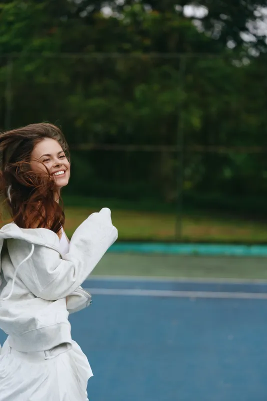Happy young woman with flowing hair joyfully running in a park, wearing a stylish white outfit, capturing the essence of freedom and enjoyment in nature