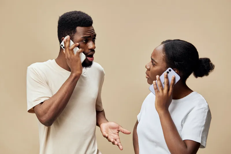 Engaged conversation between an African couple using smartphones against a soft beige background, showcasing modern communication and connection