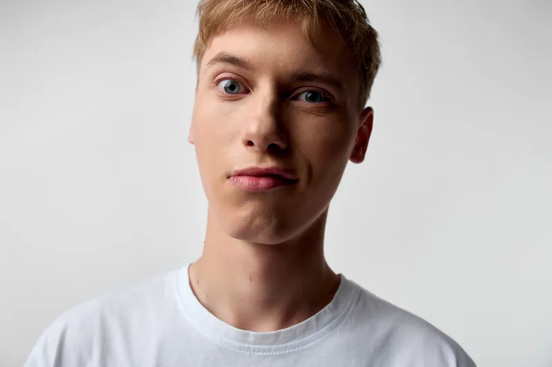 Young man in a studio with neutral background, close up of the face and calm expression, white shirt, clean lighting, focusing on mood, features and subtle details of skin tone