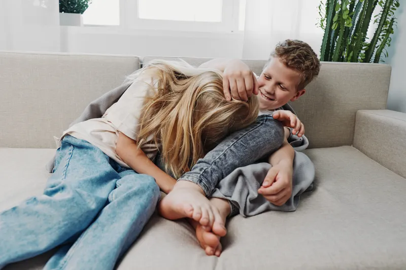 Happy children playing together on a sofa in a bright room, laughing and enjoying a playful moment. Concept of family bonding, childhood joy, and sibling love in a casual home setting.