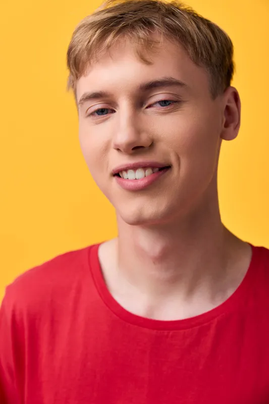 Young man, smiling, casual, red shirt against a bright studio background, presenting friendly charm, modern style and optimistic mood for lifestyle, fashion or advertising visuals