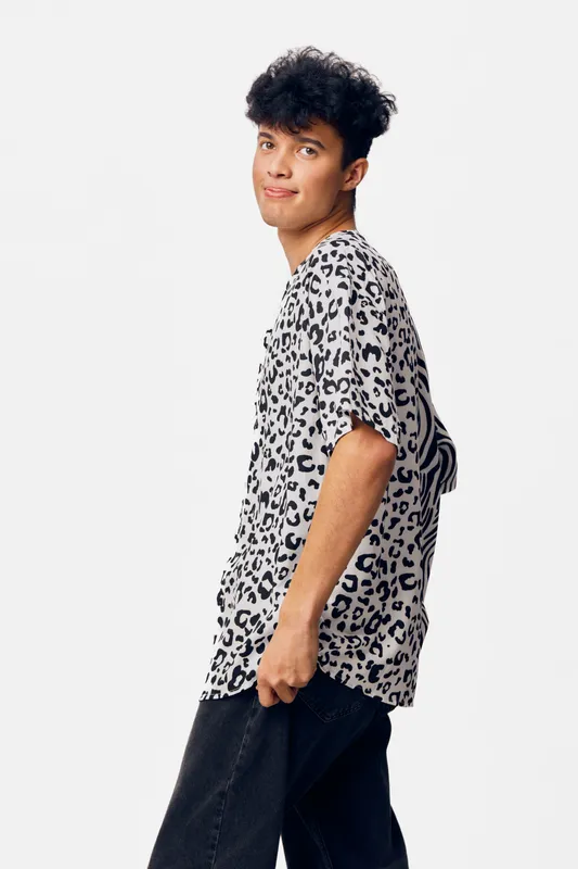 Young man wearing a leopard print shirt poses casually against a white background, showcasing trendy fashion with a relaxed and playful expression.