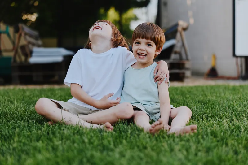 Joyful boys sitting on grass, laughing together, showcasing friendship and childhood innocence in a natural outdoor setting. Perfect for family-oriented themes.