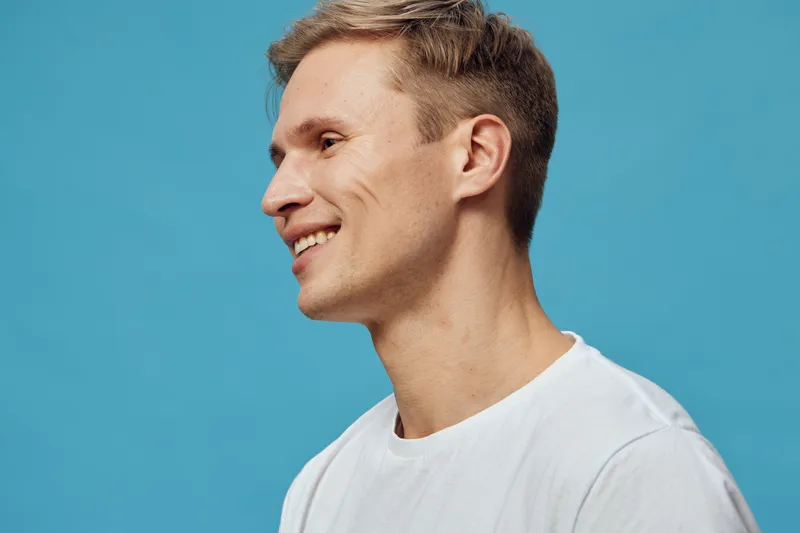 smiling young caucasian man profile view wearing white t-shirt looking away isolated on blue background digital nomad concept